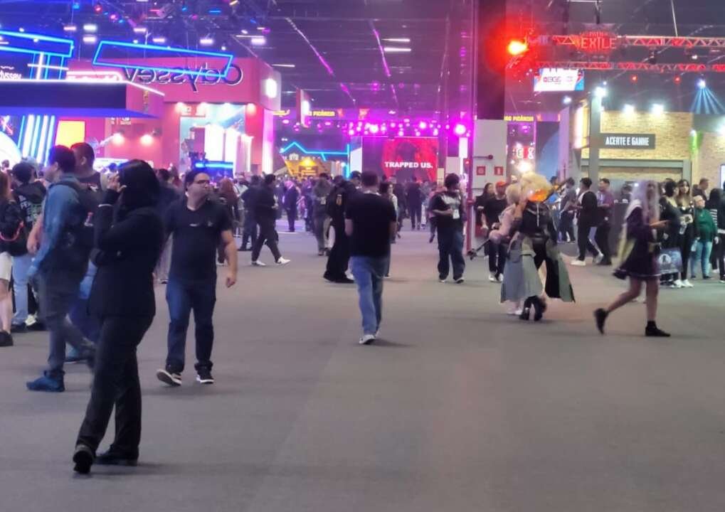 Uma visão geral do pavilhão do Distrito Anhembi. Muitas pessoas transitam pelos corredores entre os diversos estandes.  